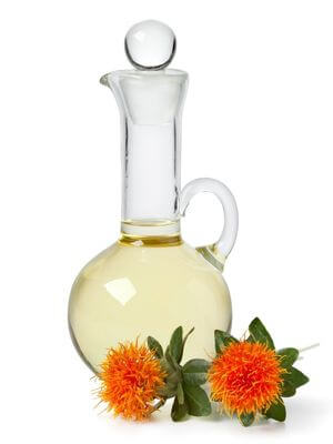 Clear glass decanter filled with light yellow safflower oil, accompanied by two vibrant orange safflower blooms with green leaves